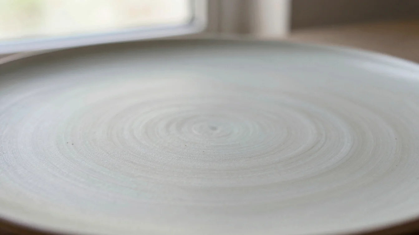 Close-up of a glazed ceramic surface with subtle variation in tone, soft window daylight, quiet background